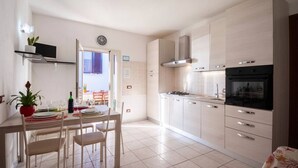 A modern kitchen with white cabinets, a dining table set with plates and glasses, and a stove. - Aricipelgo - Ponza apartment (Marina di Campo)