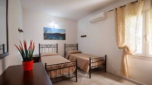 A room with two single beds, a small table with a red pot, a painting on the wall, and a window with curtains. - Aricipelgo - Ponza apartment (Marina di Campo)