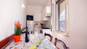 Un coin repas avec une table dressée pour deux personnes, une plante en pot et une bouteille de vin.