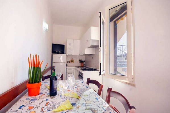 A dining area with a table set for two, a potted plant, and a bottle of wine.