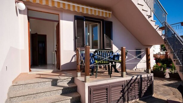 Un bâtiment doté d’un escalier menant à une porte, d’un balcon avec une balustrade et d’un petit espace extérieur aménagé pour s’asseoir.