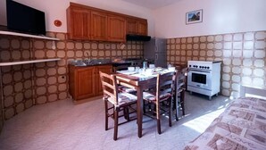 A compact kitchen with wooden cabinets, a stove, and a dining table with chairs.