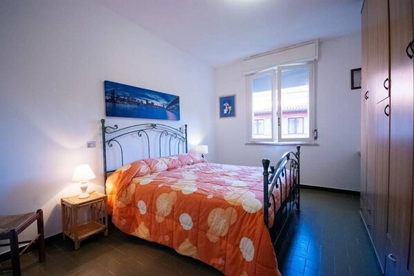 A bedroom with a bed, a nightstand, a chair, a window, and a door.