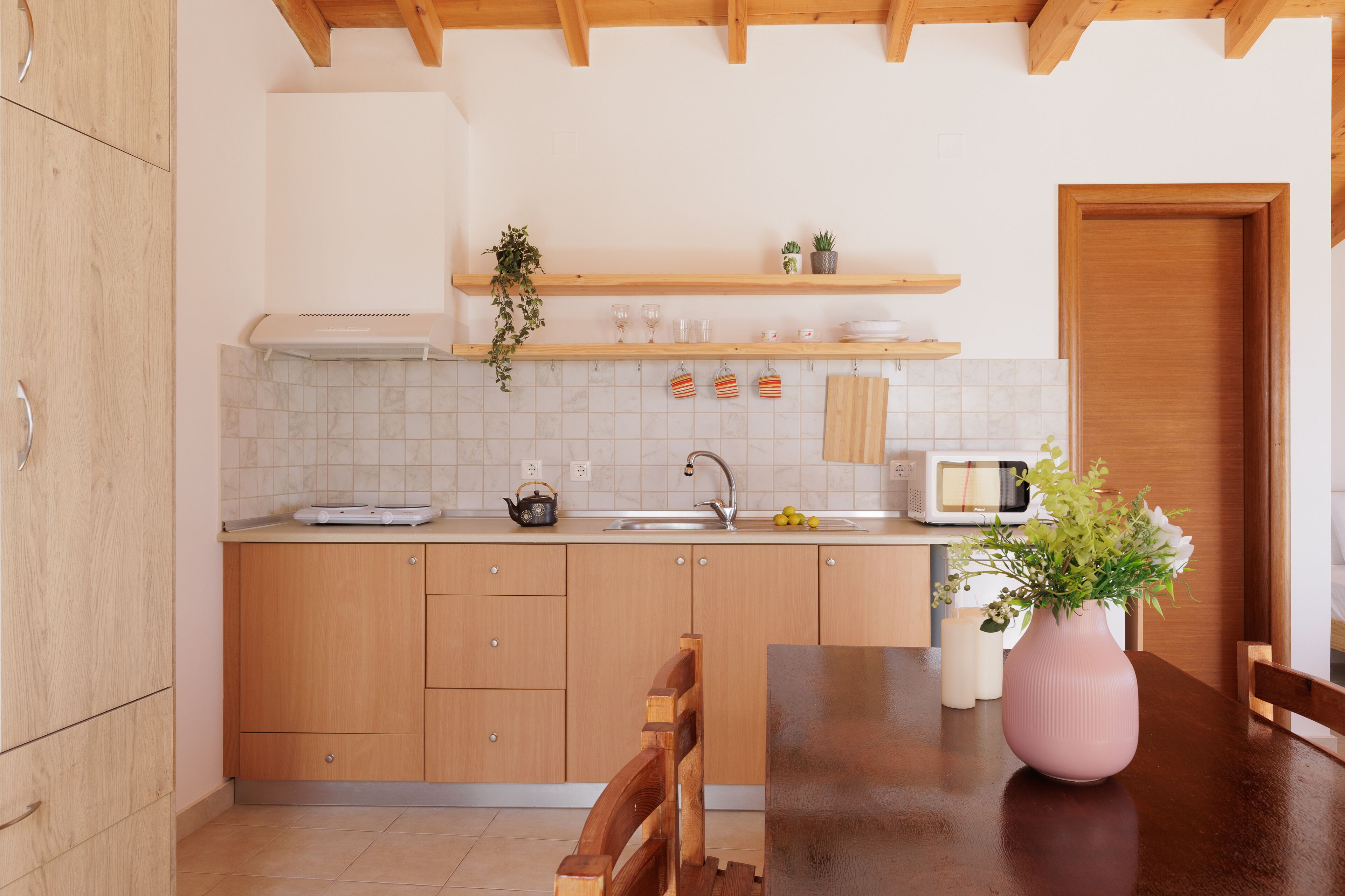 A modern kitchen with wooden cabinets, a countertop, a sink, a microwave, and a vase with flowers.