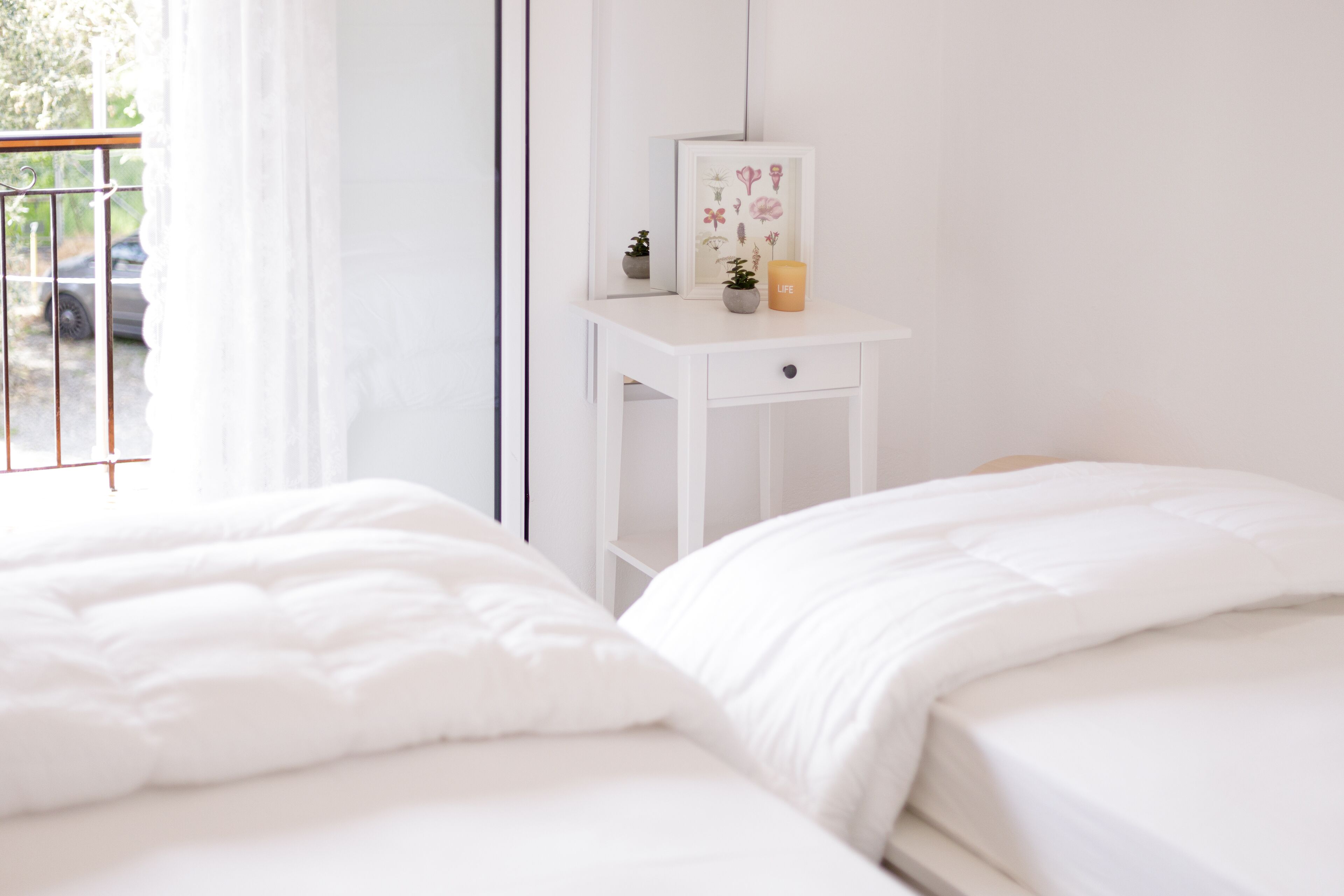 Una camera da letto con due letti, un comodino con una cornice e una finestra che si affaccia su un'auto.