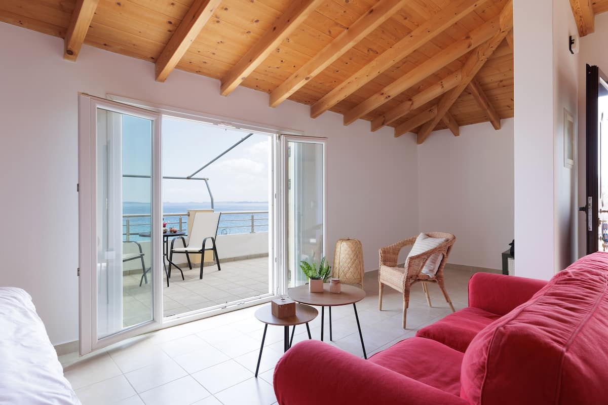 A modern room with a wooden ceiling, a large sliding glass door to a balcony, a red sofa, and a small round table with a plant.