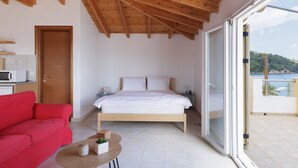 Een slaapkamer met een houten plafond, een bed, een rode bank, een klein tafeltje met een plant en uitzicht op zee door een schuifdeur.