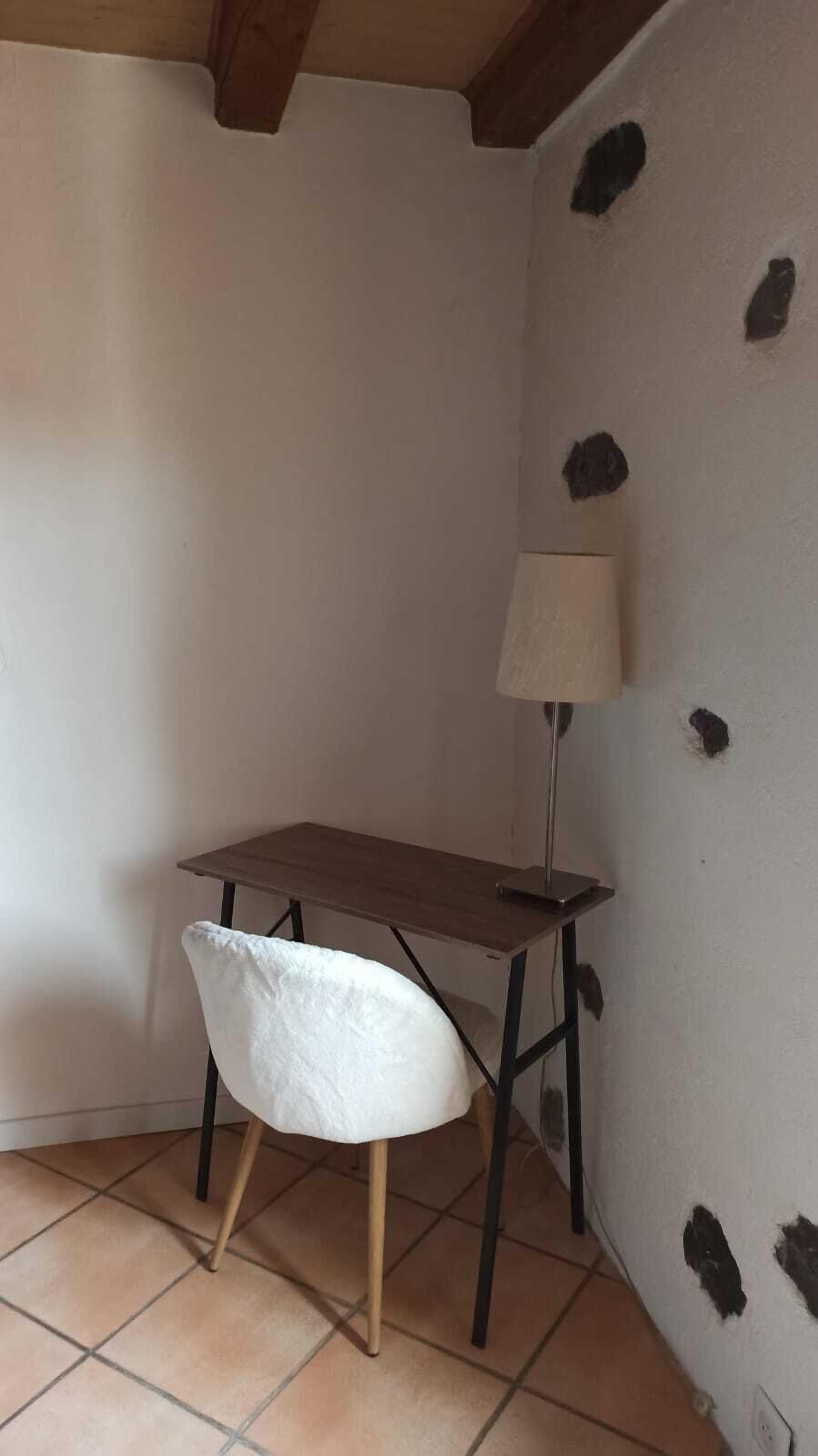 A small, cozy room with a wooden table, a white chair, and a floor lamp.
