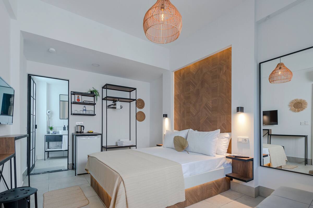 A modern hotel room with a large bed, a TV, a desk, and a bathroom visible through an open door.