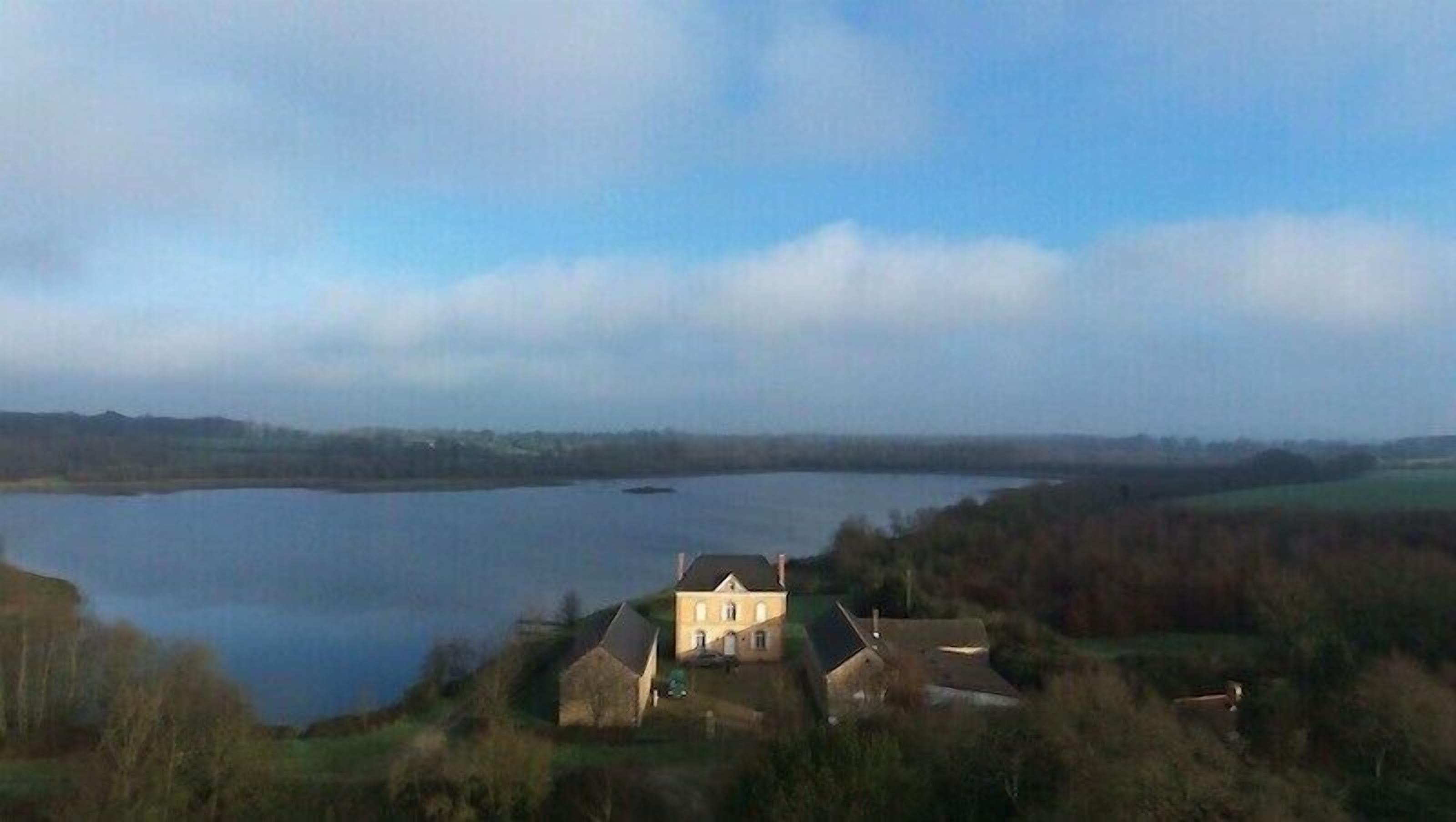 A large house with a symmetrical facade, situated on a hill overlooking a lake.