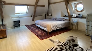 A bedroom with a wooden ceiling, a bed, a radiator, a window, and a zebra rug. - A haven of peace and nature (Sainte-Suzanne-et-Chammes)