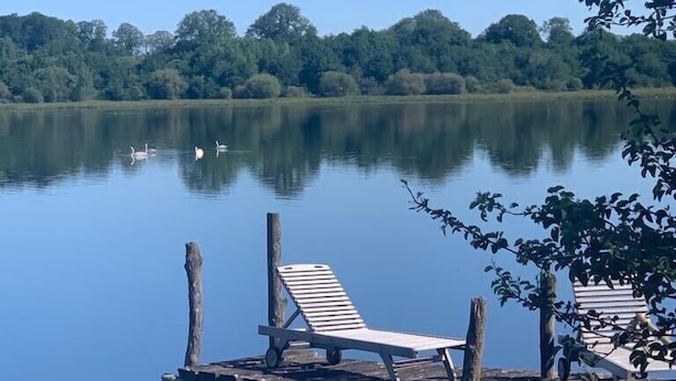 A wooden dock with two lounge chairs extending over calm water, surrounded by lush greenery and trees in the background. - A haven of peace and nature (Sainte-Suzanne-et-Chammes)