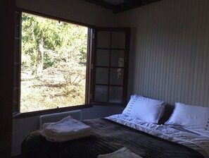 Enjoy a peaceful retreat with a view of the surrounding woods from this cozy room featuring a comfortable bed and traditional architectural details.
