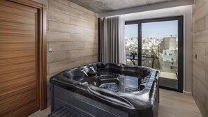 Un baño moderno con suelo de madera, un ventanal con vistas a la ciudad y una bañera negra.