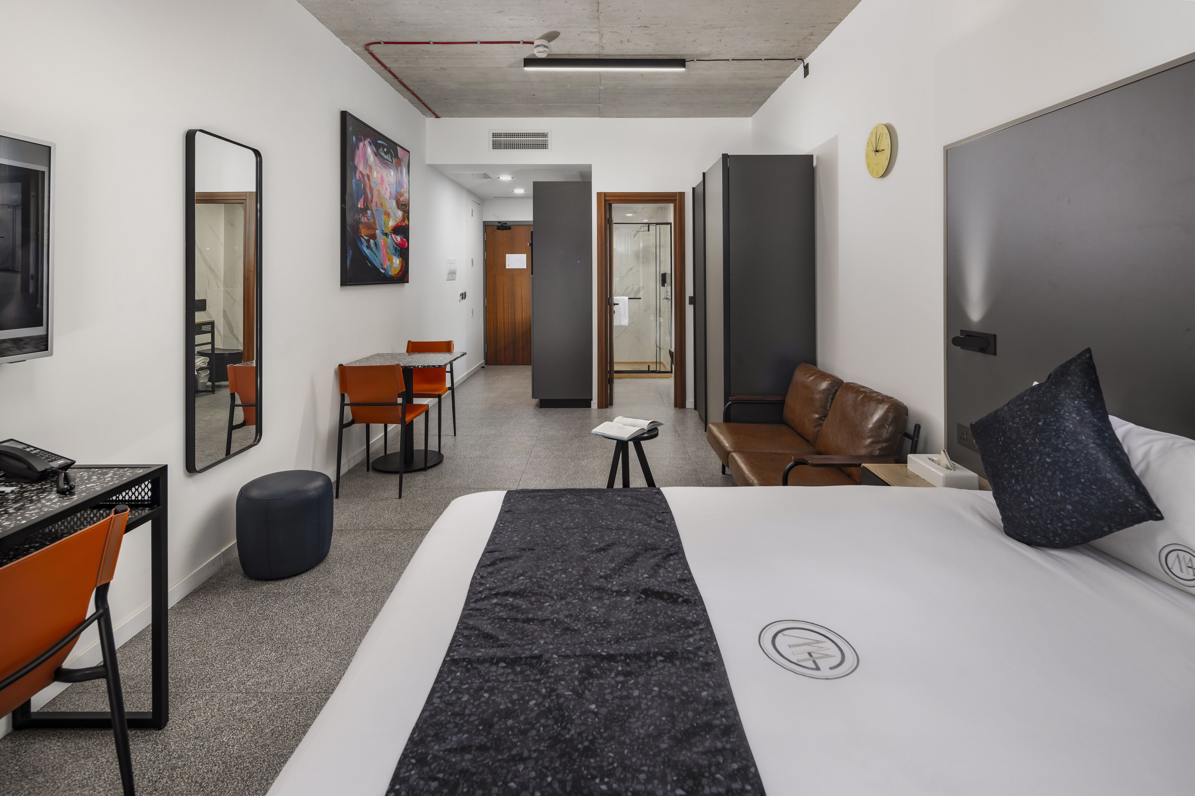 A modern hotel room with a bed, a desk, a chair, a sofa, and a small table.