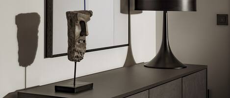 A modern interior with a minimalist design, featuring a dark-toned cabinet, a sculptural piece, and a framed artwork on the wall.