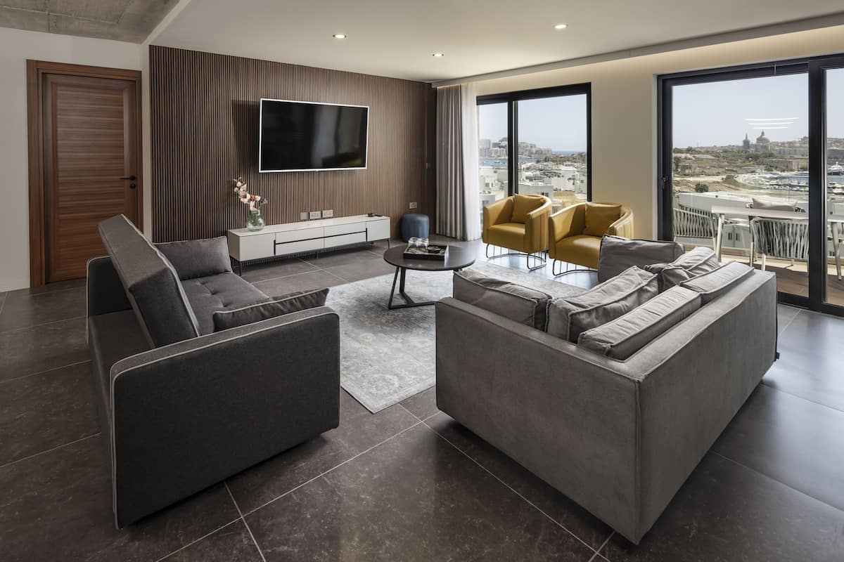 A modern living room with a large flat-screen TV, a sofa, a coffee table, and a yellow armchair.