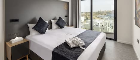 Habitación de hotel moderna con una cama grande, una mesita de noche y vistas de la ciudad a través de un amplio ventanal.