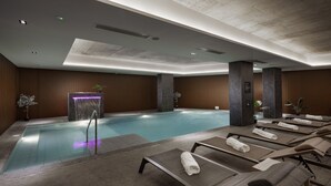 Un área de piscina interior moderna con sillones de descanso y una fuente de agua.