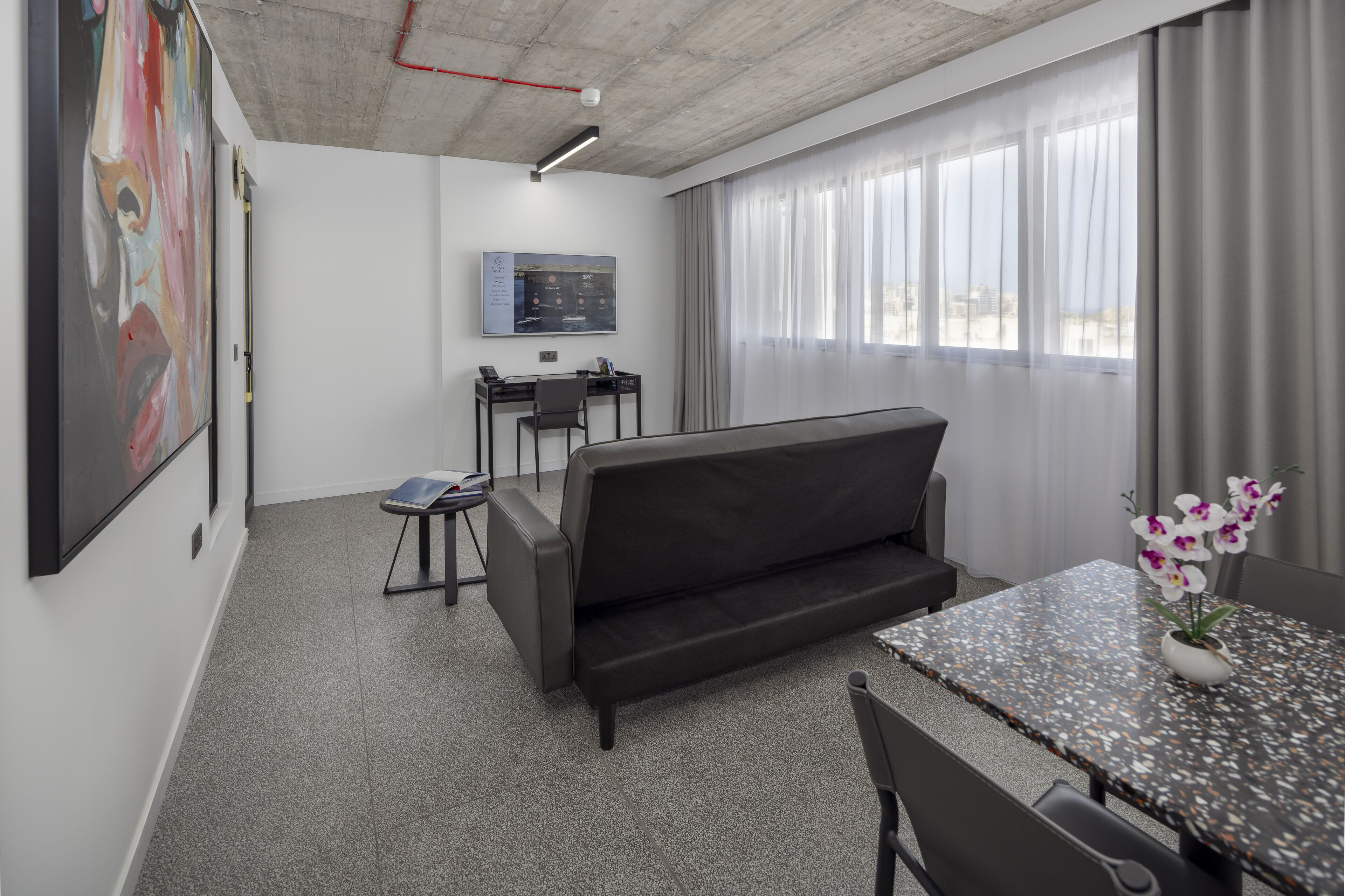 Un espacio de oficina moderno con sofá, escritorio y silla. Hay un cuadro en la pared y una ventana con cortinas.