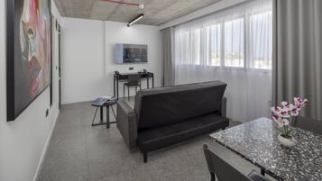 Un espacio de oficina moderno con sofá, escritorio y silla. Hay un cuadro en la pared y una ventana con cortinas.