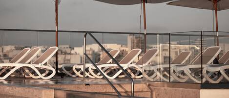 Zona de piscina en la azotea con sillas de descanso y sombrillas, con vistas a la ciudad.