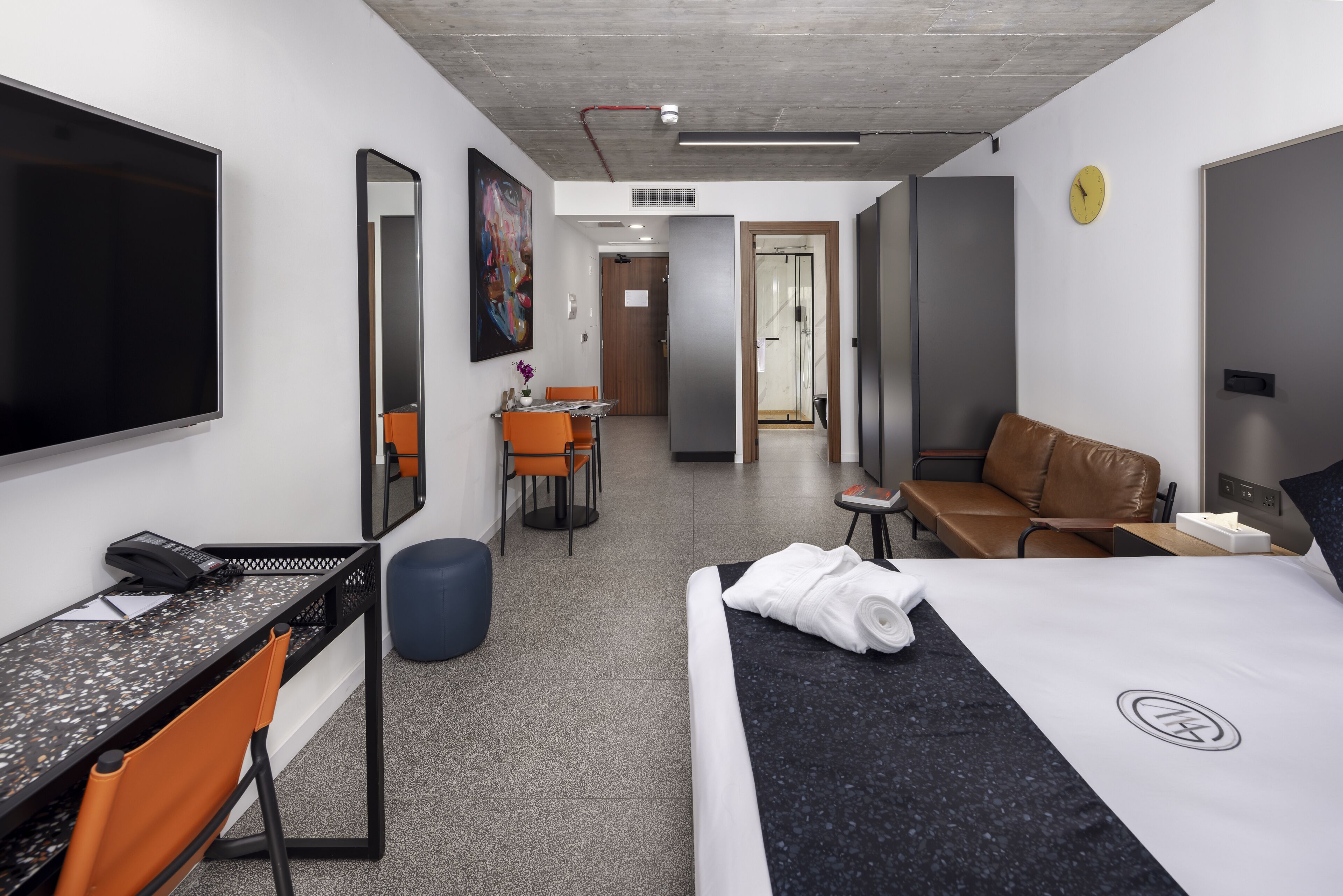 A modern hotel room with a bed, desk, chair, and a small seating area.