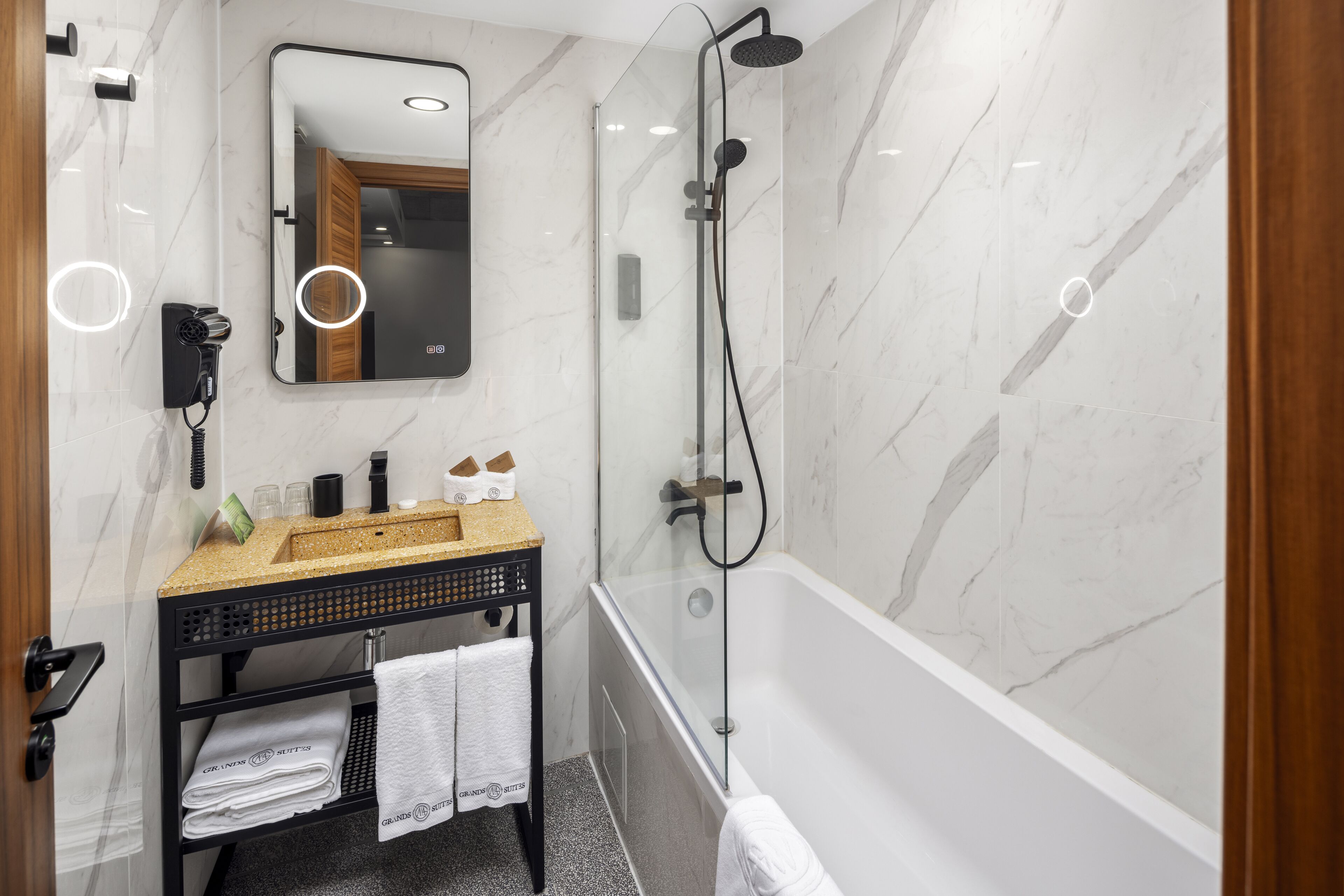 Ein modernes Badezimmer mit Marmorwand, einer Glaskabine für die Dusche, einem Waschbecken mit Handtuchhalter und einem Fön.