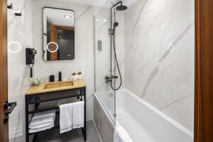 Un baño moderno con pared de mármol, ducha con cerramiento de vidrio, lavabo con toallero y secador de pelo.