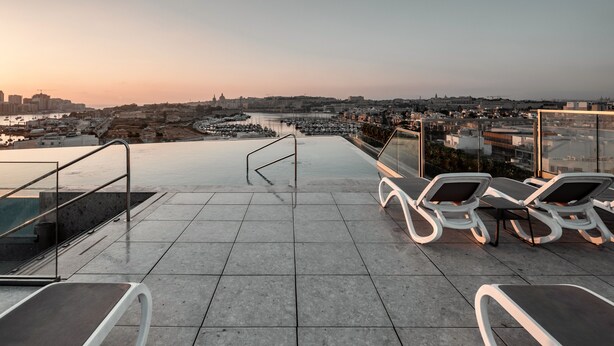 Terraza en la azotea con sillones de descanso y vistas a un paisaje urbano al atardecer.