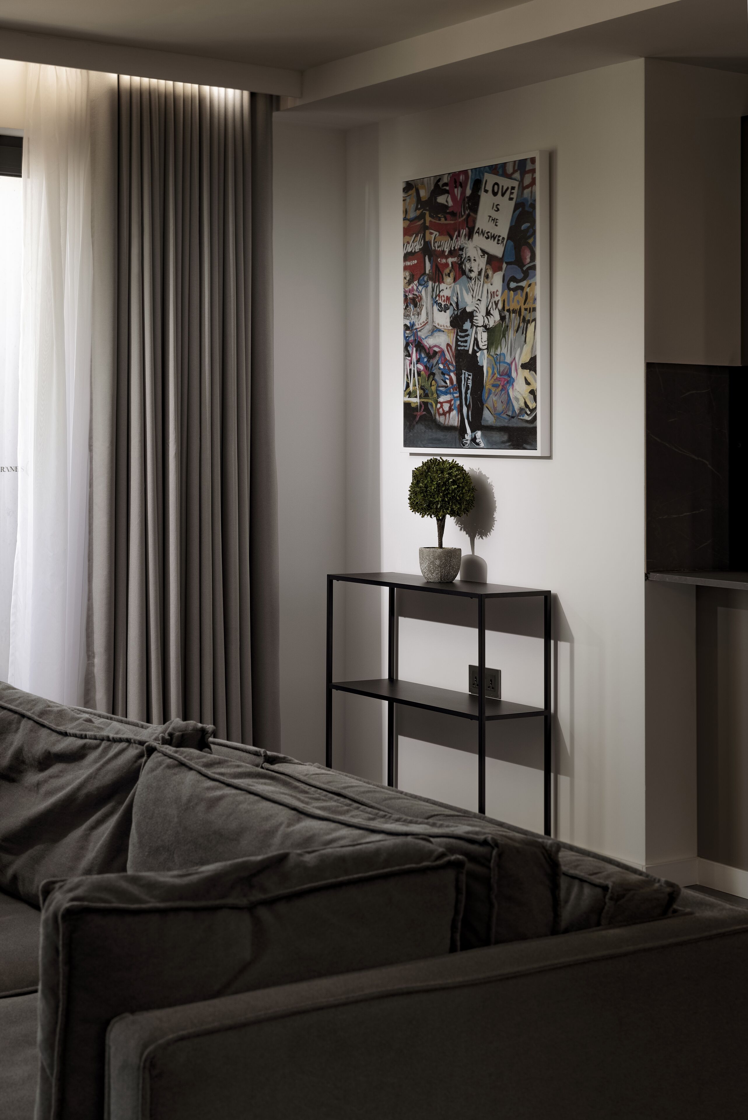 Una sala moderna con un sofá gris, un mueble de televisión negro con una pequeña planta en maceta y una llamativa obra de arte al estilo graffiti en la pared.