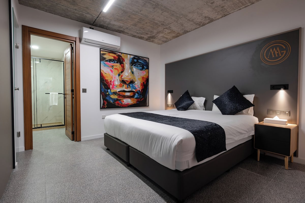 A modern bedroom with a large bed, bedside lamps, and a colorful painting on the wall.