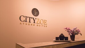 En receptionsdisk med et skilt der viser "CITYZOE ATHENS SUITES" og en logo over den.