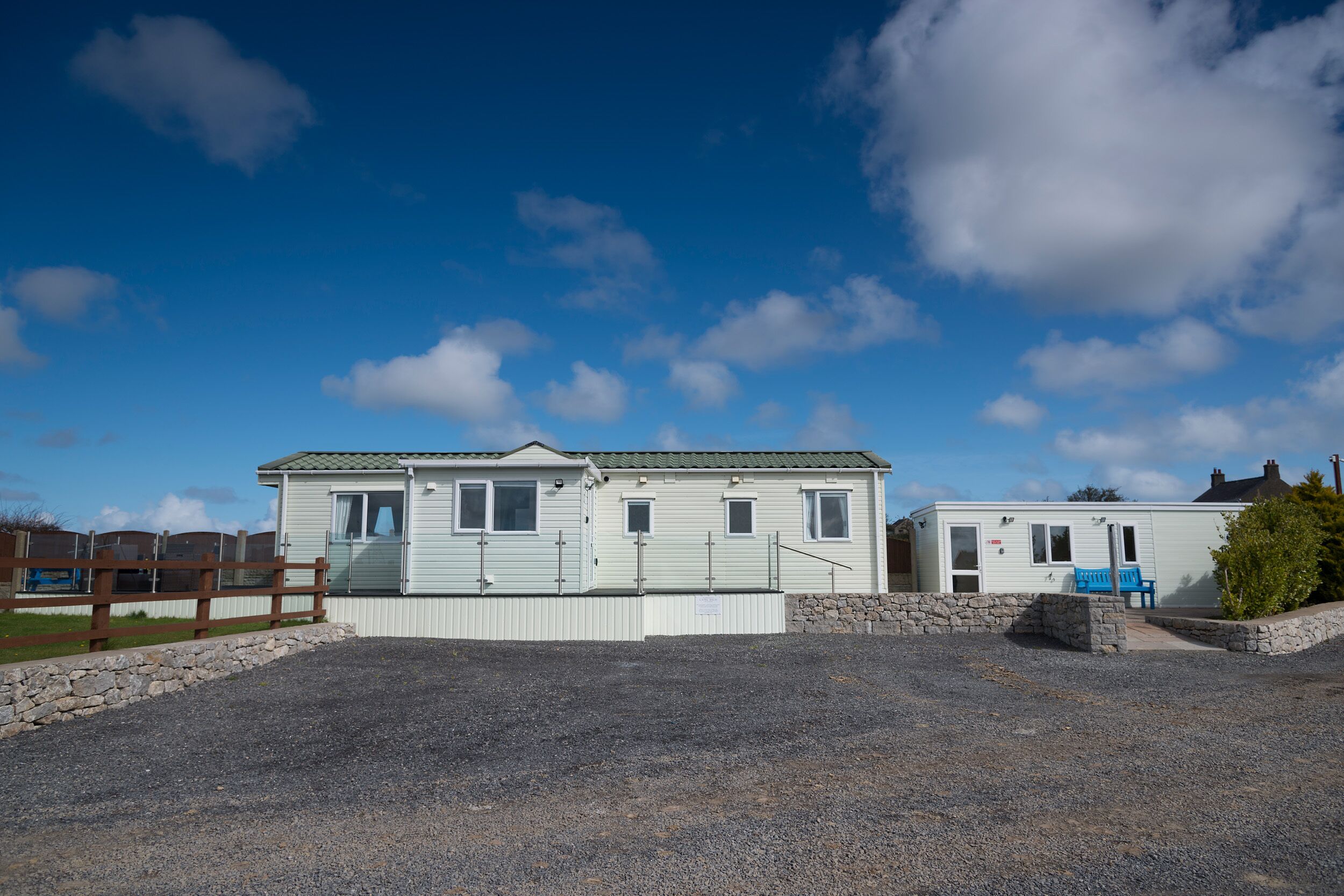 A mobile home with a gravel driveway and a wooden fence.