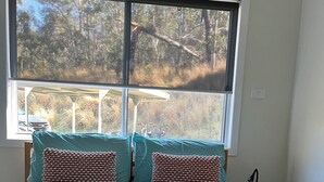 Un lit avec une tête de lit en osier, deux oreillers à motifs et une vue sur les arbres par la fenêtre.