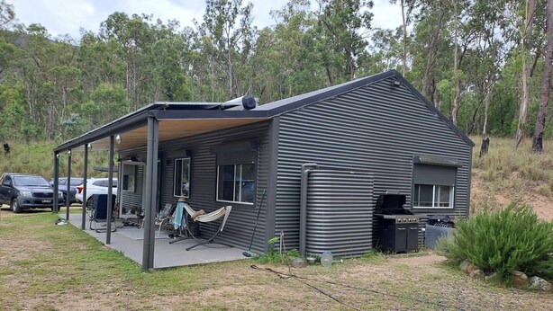 Une cabane moderne de plain-pied, dotée d’un porche couvert, d’un barbecue et d’un petit espace de détente extérieur.