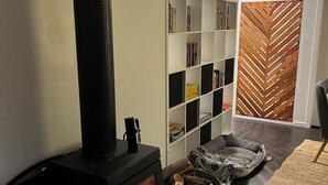 Un salon moderne avec un poêle à bois, une bibliothèque et un panier pour animaux de compagnie.