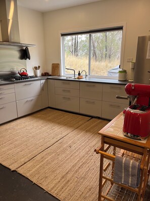 A kitchen with a gas stove, a red toaster, and a window with a view of trees.