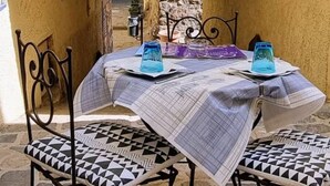 Un espace extérieur aménagé avec une table pour deux, situé sous une arche, avec des murs en pierre et une vue sur la rue.