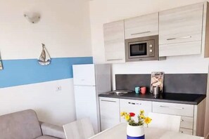 Una cocina compacta con microondas, un lavamanos y un pequeño comedor con una mesa y un florero.