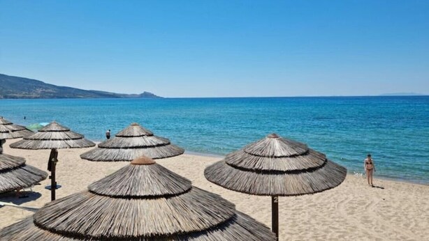 Une plage avec des parasols en chaume et une mer d’un bleu limpide.