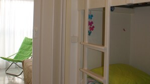 Una cama litera infantil con ventana, una silla verde y una puerta que da a otra habitación.