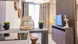 A modern living room with a flat-screen TV, decorative wall art, and a large window with curtains. - Evitel Luxury Living (Kassandra)