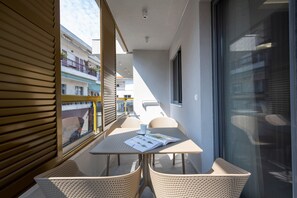 A balcony with a table, chairs, and a window overlooking a building. - Evitel Luxury Living (Kassandra)