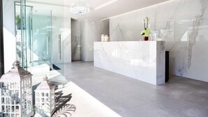 A modern reception area with a marble reception desk, a chandelier, and a glass door leading to a shower area. - Evitel Luxury Living (Kassandra)