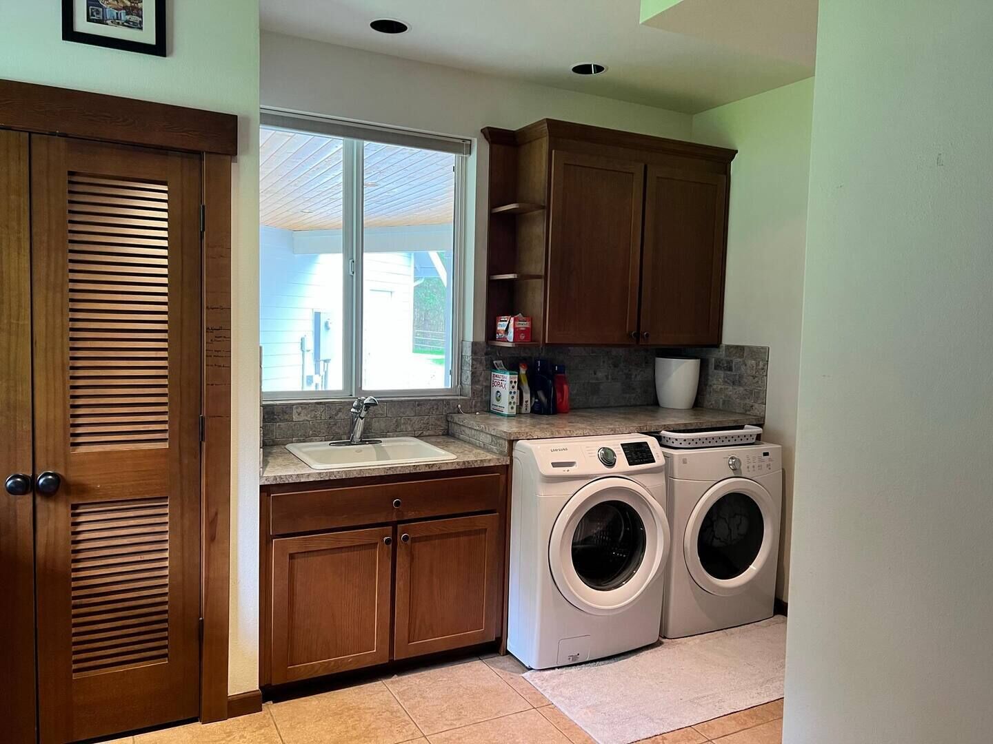 A compact laundry room with a sink, wooden cabinets, and two front-loading washing machines.