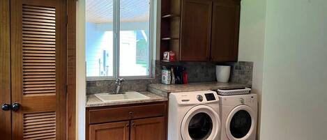 A compact laundry room with a sink, wooden cabinets, and two front-loading washing machines.
