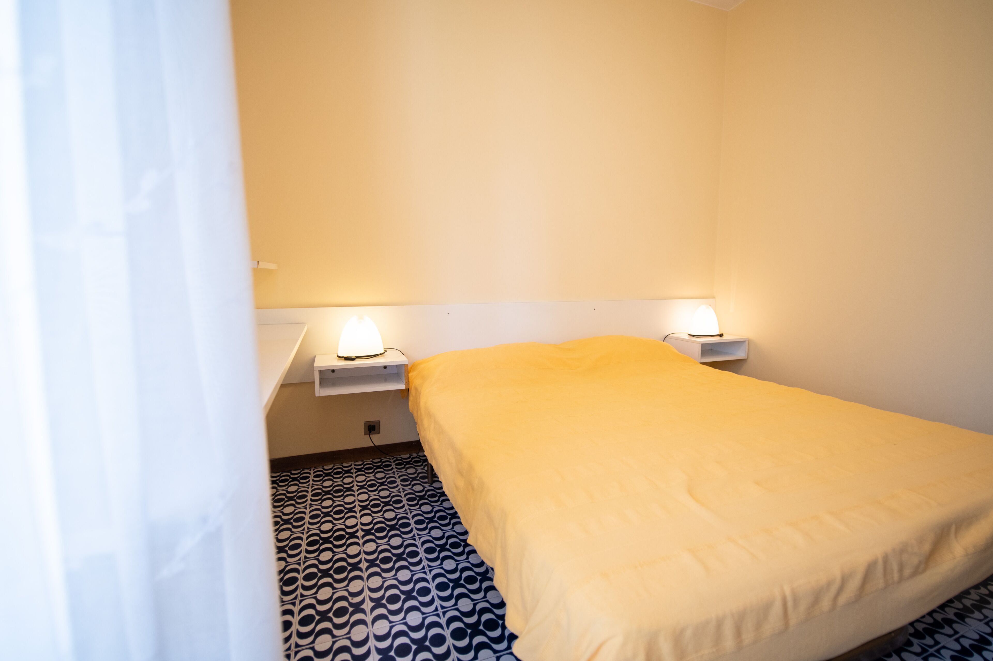 Une chambre d’hôtel avec un lit, deux tables de chevet avec des lampes et des carreaux de sol à motifs.