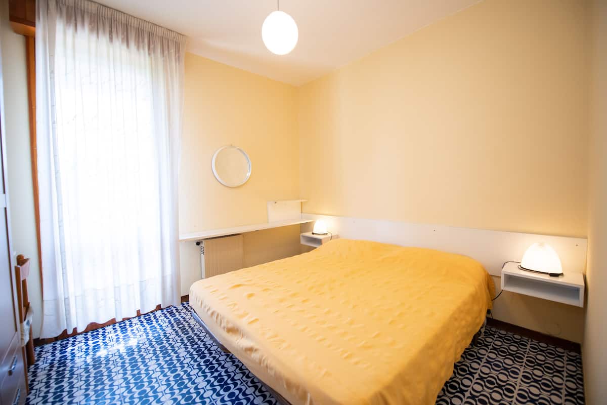 Een hotelkamer met een bed, een nachtkastje met een lamp, een ronde spiegel aan de muur en een vloer met een patroon.