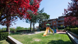 A playground with a yellow slide, surrounded by grass and trees with red leaves. - Appartamento Luisa e Francesco (Peschiera del Garda)